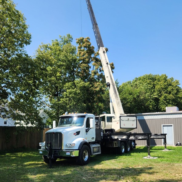Crane truck with outriggers and lawn protection mats positioned for tree removal in residential area