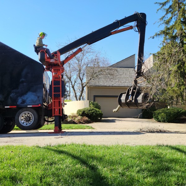 Operator using a grapple claw truck to load tree debris from a residential driveway