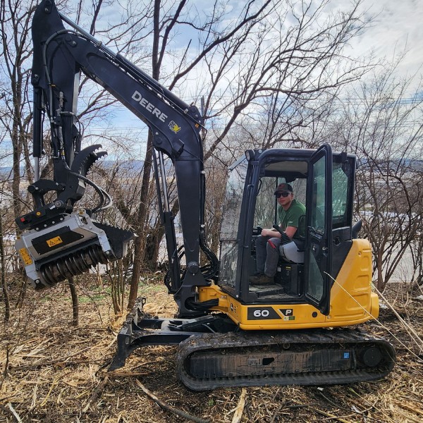 Operator running a tracked excavator with a mulcher attachment to clear brush on a hillside